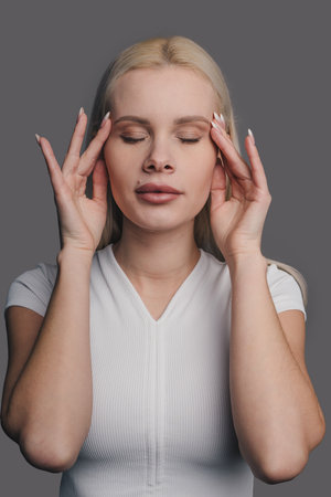 Young beautiful woman with perfect skin massaging her face holding hands on temples, doing massage movements on her face. Anti-aging concept, smoothing, rejuvenating beauty treatmentの写真素材