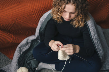 Top view of a beautiful young woman in casual wear sitting on the floor at home knitting with crochet. Relax, carefree, comfort lifestyle.の写真素材