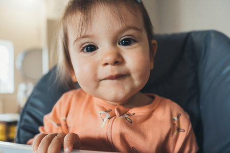Close-up portrait of a baby girl sitting on a high chair ready to eat. Everyday lifestyle.の写真素材