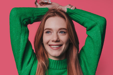 Close-up portrait of nice charming attractive red-haired woman posing with her hands over her head while looking away on a studio background.の写真素材