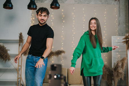 Smiling female and male influencer shooting trendy dance video for social media, using mobile phone screen on tripod stabilizer. New content for blog while streaming online. New digital trend conceptの写真素材