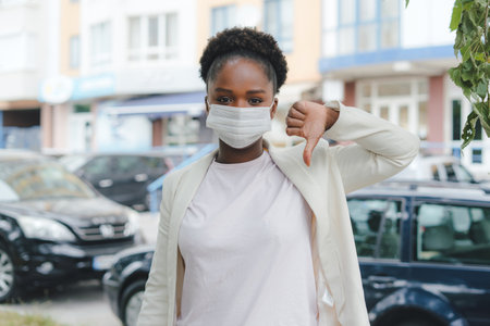 Discontent African American woman wearing medical mask showing dislike with thumbs down, rejection concept. Concept of coronavirus, quarantine and social distancing.の写真素材