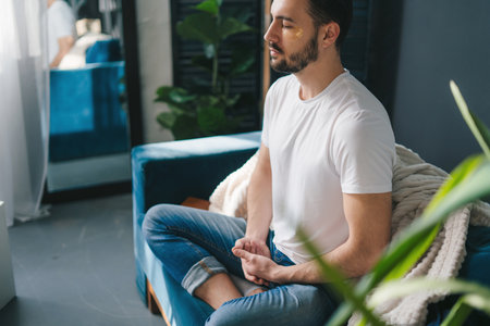 Photo of a young man doing yoga and meditating on the living room comfortable sofa. Morning relaxation and yoga practice conceptの写真素材