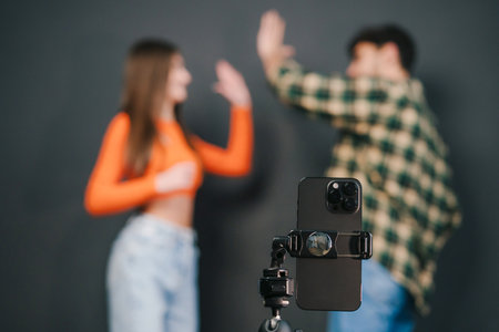 Portrait of two gen Z teenagers giving high fives while filming video for social media isolated over black background. For lifestyle design. Video live streaming.の写真素材