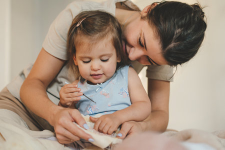 Young attractive woman with brunette hair sitting on the floor spending time with her baby girl...