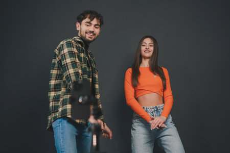 Two young friends having fun recording video reels with mobile phone for social media isolated over black background. Teen trends lifestyle concept. Internet technology, digital marketing. Marketing technology. Video live streaming.の写真素材