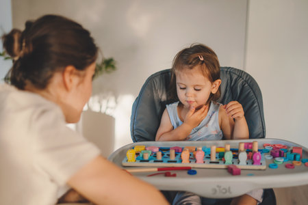 Happy caucasian baby girl sitting on high chair and playing with educational wooden toy. Concept of early learning and development of fine motor skillsの写真素材