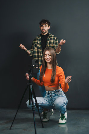 Funny couple recording video for social media dancing in front of camera, modern cell phone on tripod, black background. Video content to share on social mediaの写真素材