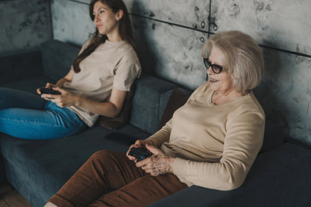 Pretty millennial women relaxing at home, resting on sofa playing video games together in a living room at home. Laughing family with happiness.の写真素材
