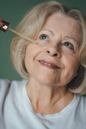 Head shot portrait smiling beautiful mature senior woman applying cosmetic oil serum on face taking care of skin. Smile face. Skin care. Modern female lifestyle. Happy lifestyle.の写真素材