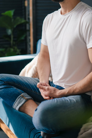 Relaxed man, sittin alone at home in living room on a sofa, meditating in the lotus position, take care of his mental health. Chilling and relaxing at home.の写真素材