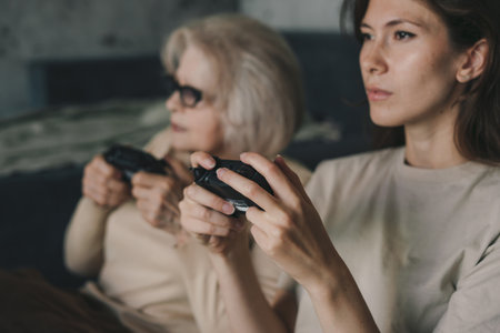Two women playing console tv games, holding the joystick sitting on the floor in living room. People...