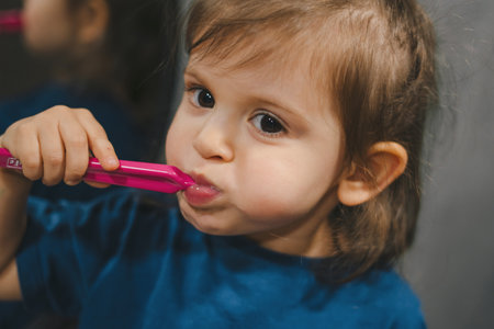 Close-up portrait of a cute little baby girl wearing blue t-shirt holding toothbrush and learn to brushing teeth in the morning at home. Tooth care for children concept. Health care.の写真素材