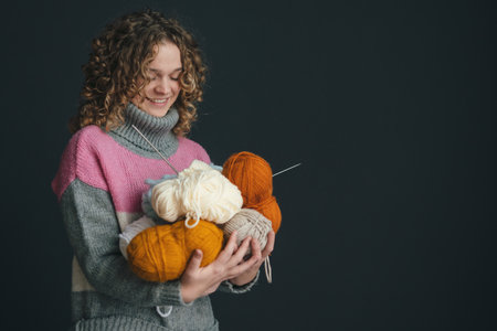 Beautiful woman with curly hair bearing many color hanks of a yarn for knitting, posing against black background with copy space. Free space for text. Hobby concept. Happiness concept. Cheerful smiling young woman. Smile emotions.の写真素材