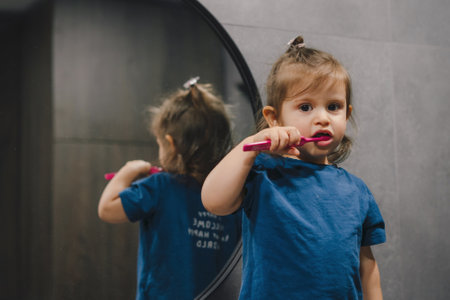 Cute caucasian baby girl brushing her teeth in the morning in the bathroom, and looking to the camera. Healthy and routine life concept.の写真素材