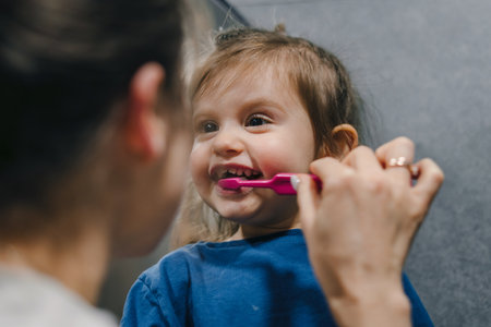 Happy mother and child little baby girl cleaning teeth with a toothbrush in the bathroom. Happy, love and care mom teaching child or kid about dentistry and cleaning mouth in morningの写真素材