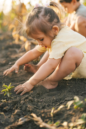 Baby small caucasian little girl sitting on the ground in bright spring day playing, childhood development learning and family concept. Baby development. Garden nature. Little garden. Summer vacation fun.の写真素材