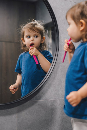 Little baby girl brushing teeth with pink toothbrush, good dental hygiene practice in childhood. Dental care. Healthy concept.の写真素材