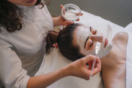 Cosmetologist applying facial cream all over young womans forehead at spa salon. Skin treatment. Girl facial treatment.の写真素材