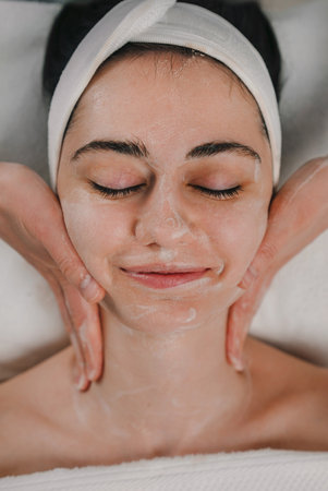 From above of young ethnic female applying moisturizing cream on faceの写真素材