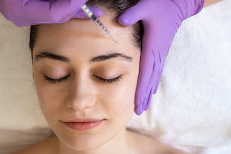Beautiful young woman getting cosmetology treatment facial skin injection by beautician in beauty clinic. Face contouring concept.の写真素材