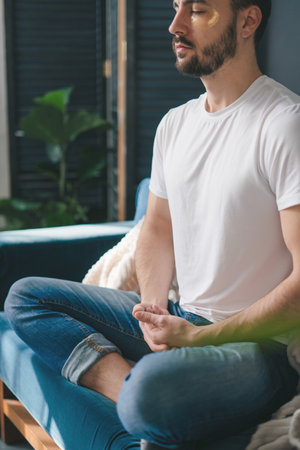 Photo of a young man doing yoga and meditating in the living room on the sofa. For concept design. Home comfort.の写真素材