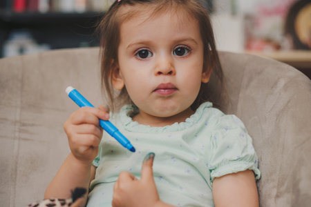 Portrait of a girl holding a blue marker and drawing her fingers, looking at camera.の写真素材