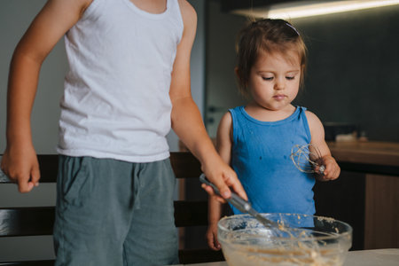 Cute little girl and her brother mixing ingredients into the bowl while preparing dough for baking. Food preparation. Kitchen interior.の写真素材