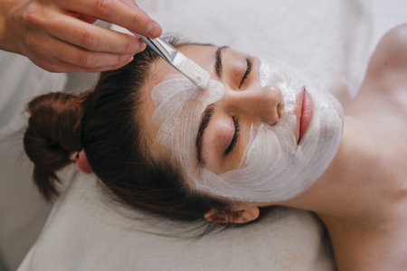 Beauticians hands covering woman facial skin with moisturizing mask during skincare procedure. Girl facial treatment. Cosmetic procedure.Beauticians hands covering woman facial skin with moisturizing mask during skincare procedure. Girl facial treatment. Cosmetic procedure.の写真素材