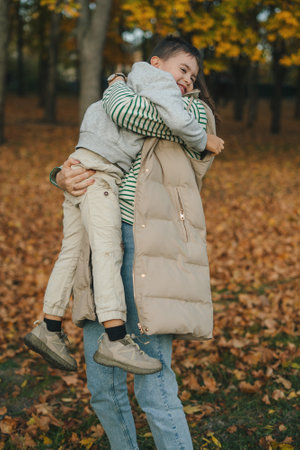 Mother and son embracing, spending time together in the autumn park. Mother hugging her son with love. Vertical photoの写真素材