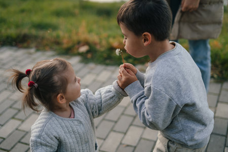 Two children, boy and a little girl, blowing on dandelion flowers in nature in summer. Child picking flowers. Children play outdoor. Nature and outdoors fun for family.の写真素材