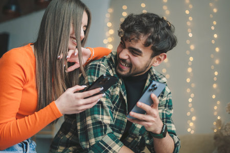 Man and woman both standing on their modern phones laughing while watching video blogs they are filming to post on social media.の写真素材