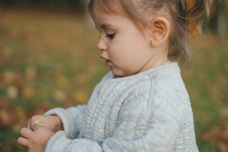 Side view portrait of a little girl admiring a small camomile holding in her hands while standing in...