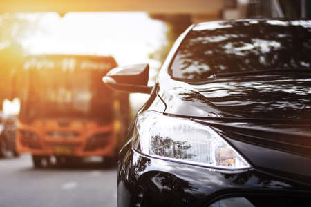 Focusing on the black car headlights on a street corner with sunlight flares. In the background, bus and car. Closeup headlights of car.の写真素材