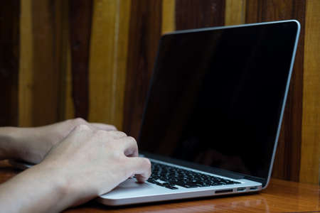 Male's hand typing on white laptop on wooden desk. work place.の写真素材