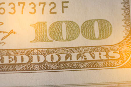 Close up on US dollar banknotes. Depth of field Number 100 on US Dollar banknotes with warm light. Shooting by 1:1 Macro lense.の写真素材