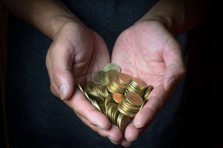 Male hand holding golden coins. Saving, money, finance donation, giving and bussiness concept. Black background. Heart shape.の写真素材
