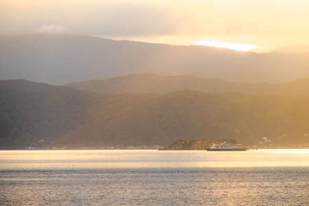 Stunning landscape sunrise in the morning. Ferry on the sea. Golden light go through the cloud to the mountain and sea.の写真素材
