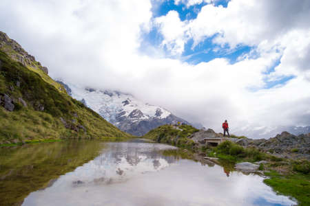 The reflection of the rocky mountain with snow and blue sky with cloud and traveller on the small...