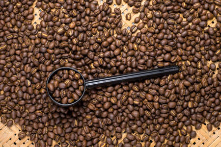 Flay lay style, Medium dark Roasted peaberry coffee beans in plastic cup spoon on bamboo handcraft background.の写真素材