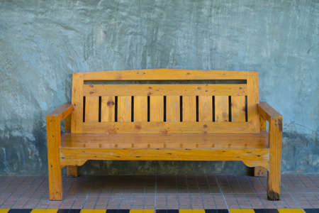 Yellow wooden bench stand beside the road with raw exposed cement wall.