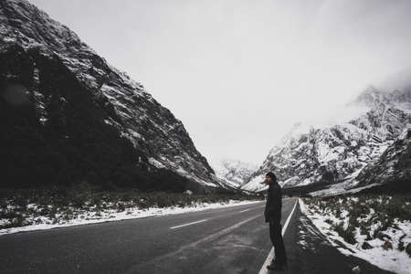 A young Asian man standing on the road among snow mountain.の写真素材