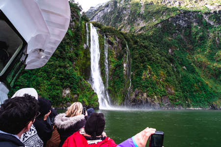A group of tourists enjoying a stunning scene of nature while cruising into waterfall in Milford Sound, New Zealand.のeditorial素材