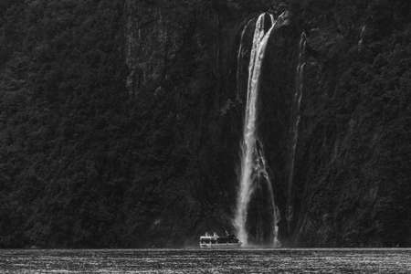 A stunning scene when a ferry cruising to a waterfall at Milford Sound, New Zealand. Black and white with high grain photo effect.のeditorial素材