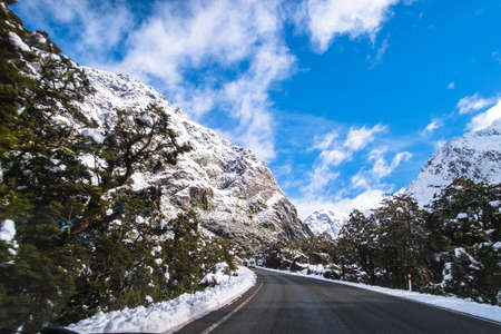 The stunning scenery of a rocky mountain and trees covered with a white snow. A road to Milford Sound. A filmed while driving.の写真素材
