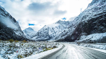 The stunning scenery of a rocky mountain and trees covered with a white snow. A road to Milford Sound. A filmed while driving.の写真素材