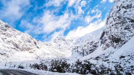 The stunning scenery of a rocky mountain and trees covered with a white snow. A road to Milford Sound. A filmed while driving.の写真素材