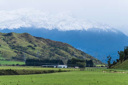 Beautiful landscape of a green meadows and snow mountain in a cloudy day. Foggy over the mountains.の写真素材