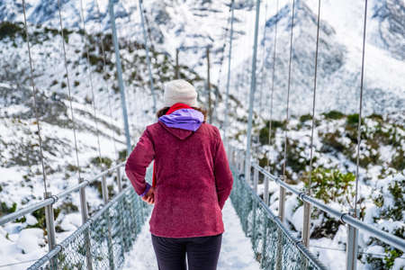 A women on the bridge crossing the river. Hooker Valley Track covered with white snow after a snowy day. Mount Cook National Park.の写真素材