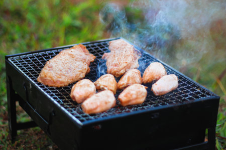 Grilled Chicken on Charcoal Stove with Smoke in Outdoor Settingの写真素材